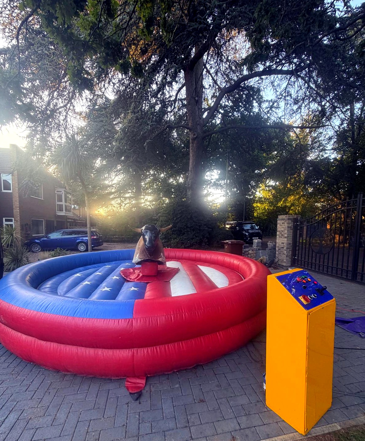 Mechanical rodeo bull in a red inflatable ring outdoors, yellow control box on the right, sunlit